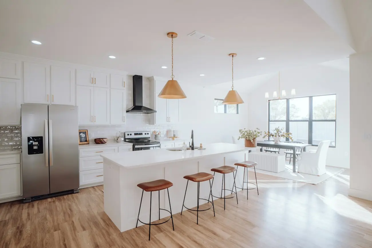 A bright white kitchen with a long island, copper pendants and oak floors