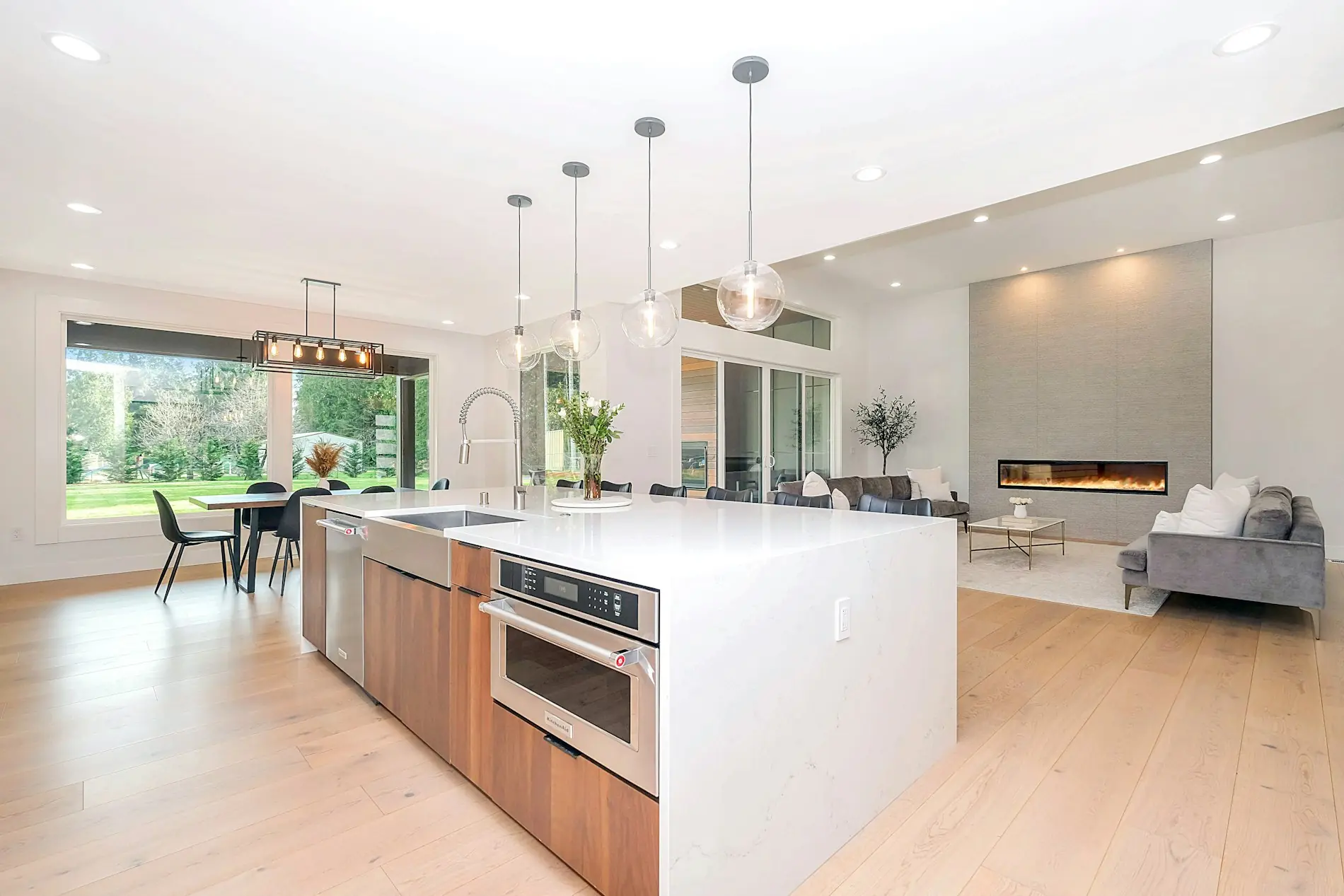 An open kitchen with a walnut and quartz island, pendant lights and a wall of glass onto the garden