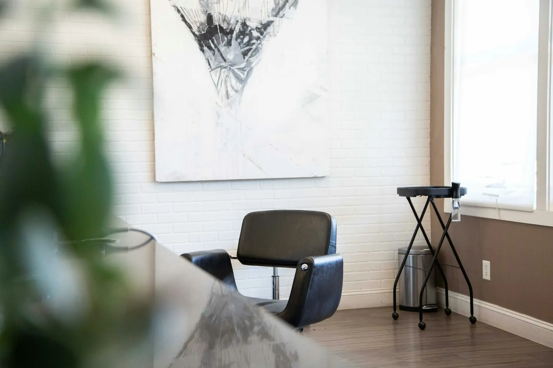 A styling chair by the window at Atelier Wren, with white brick walls and a large print